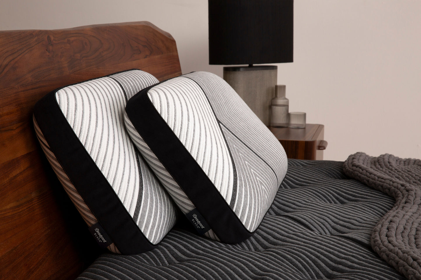 Two Beautyrest Black Black pillows sitting against a brown headboard and sitting on beautyrest black mattress
