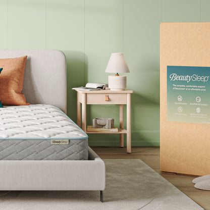 Beautysleep Mattress in a grey bedframe with 3 pillows on top of it within a bedroom setting with BeautySleep packaging to the right of it.