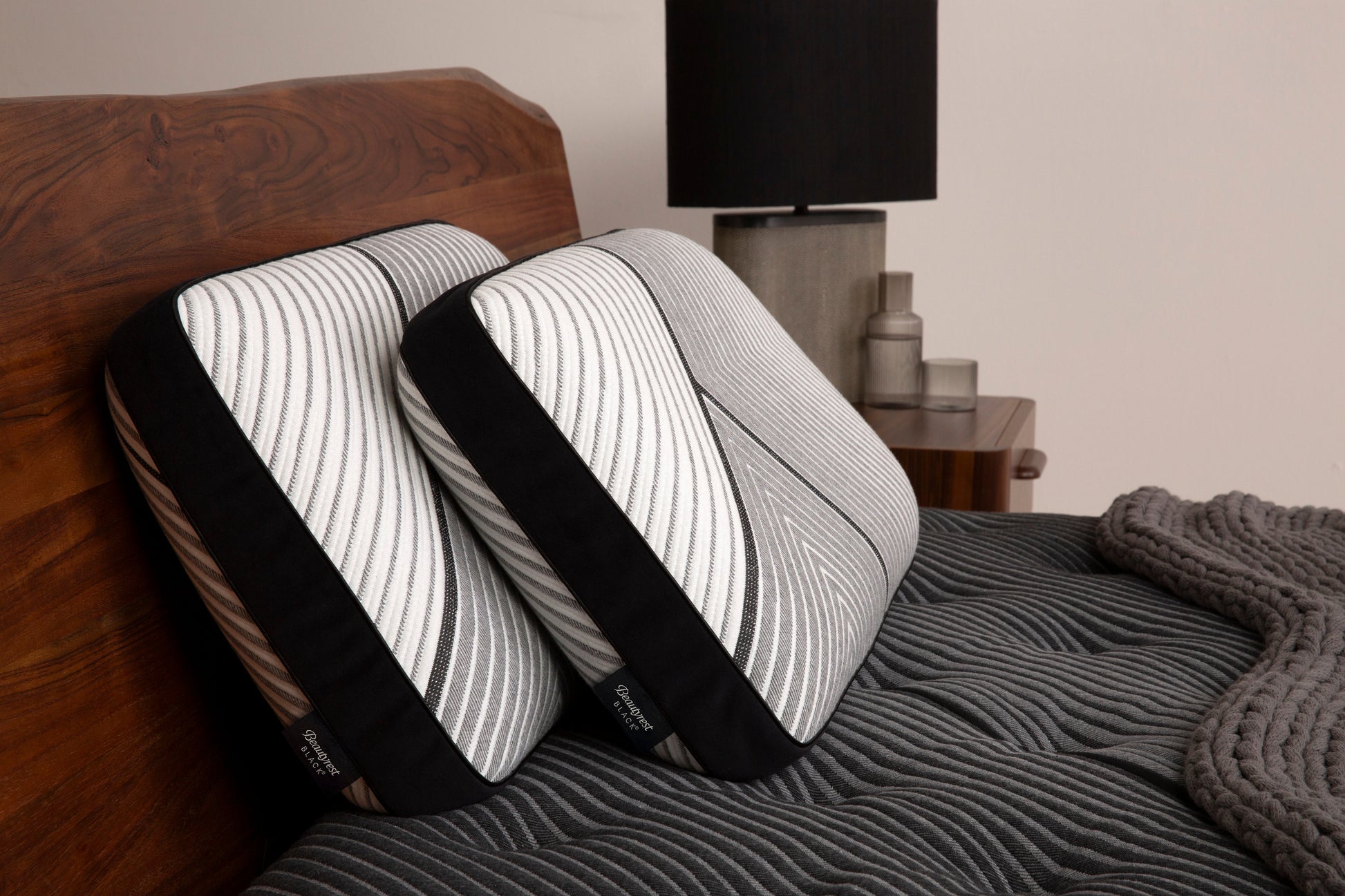 Two Beautyrest Black Black pillows sitting against a brown headboard and sitting on beautyrest black mattress