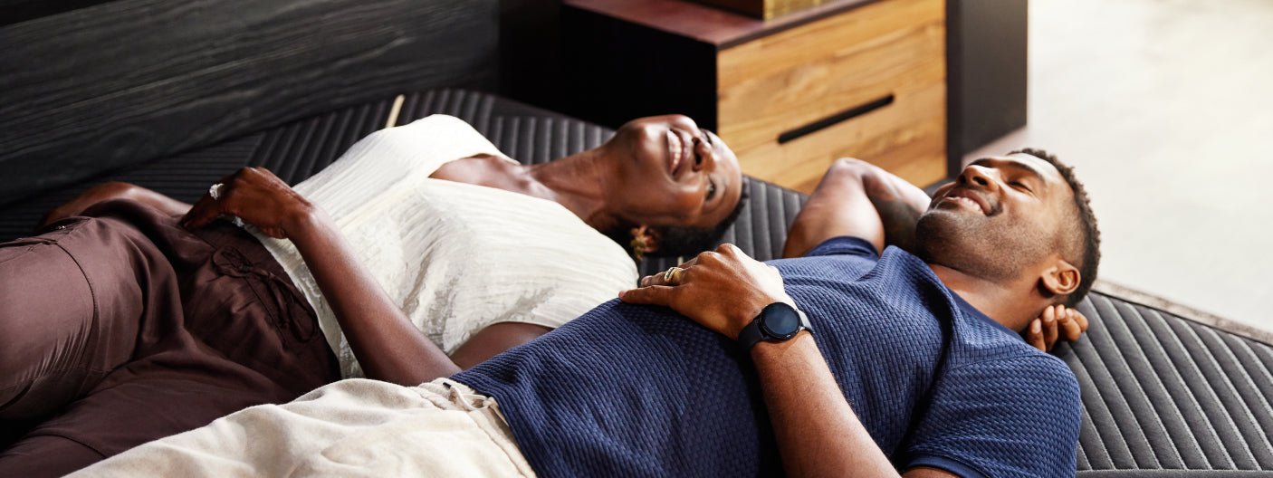 A couple happily laying down on a Beautyrest Black mattress on their backs and relaxing.